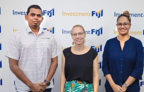 Three professionals stand before an investment Fiji sign, promoting peer-to-peer learning for Australia-Fiji trade investment.
